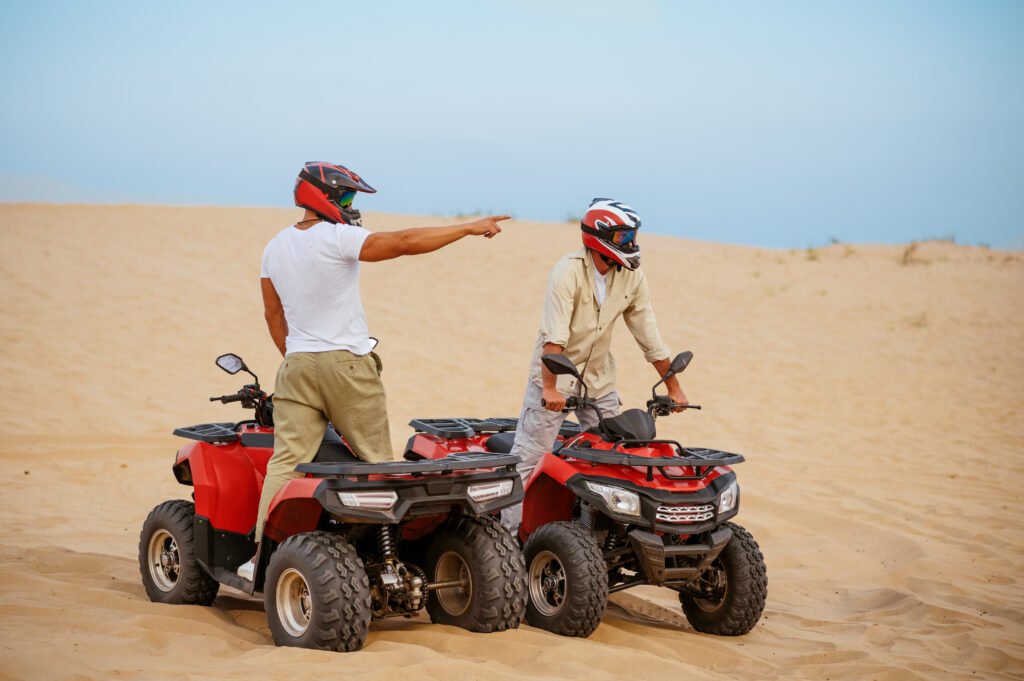 Two men in helmets, atv riding in desert sands