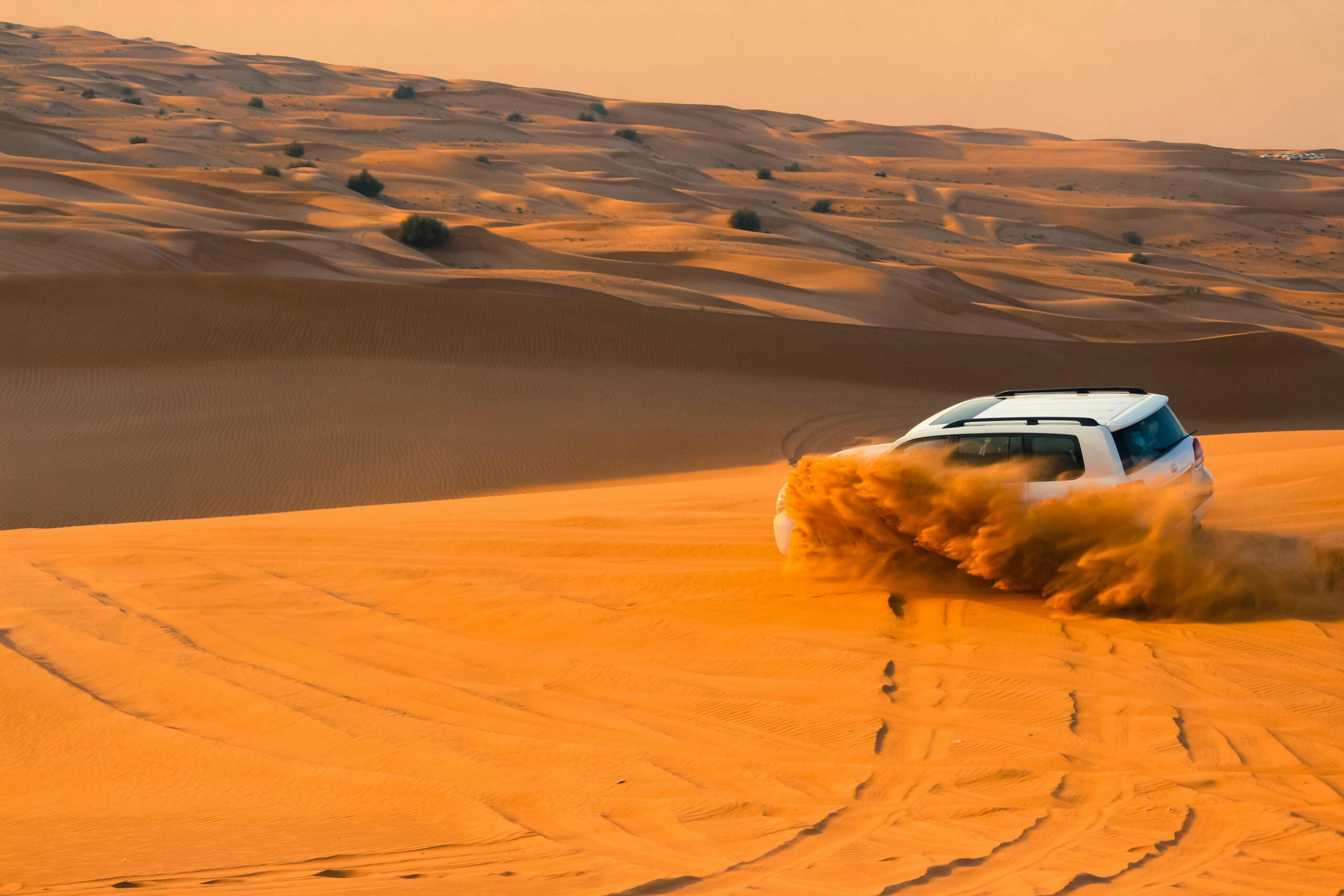 White 4x4 SUV kicking up sand while driving through the golden dunes during a private desert safari in Dubai.